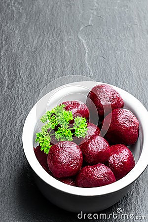 Homemade pickled baby beetroot in clay pot on black stone background Stock Photo