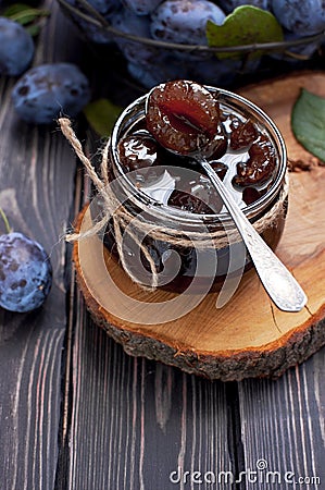 Homemade plum jam in a glass jar and fresh blue plums in a bowl on a dark rustic wooden background with copy space top view. Stock Photo