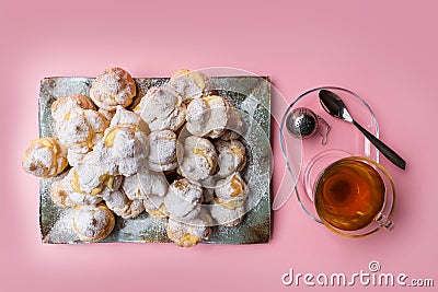 Homemade profiteroles served on a plate with a cup of tea on a pink background. Flat lay. Stock Photo