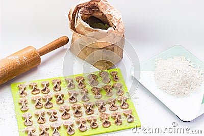 Homemade raw farfalle pasta on cutting board, rolling pin, craftpaper bag of flour and kitchen scale. Pasta of whole grain flour Stock Photo