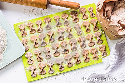 Homemade raw farfalle pasta on cutting board, rolling pin, craftpaper bag of flour and kitchen scale. Pasta of whole grain flour Stock Photo