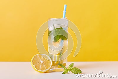 Homemade refreshing summer lemonade drink with lemon slices, mint and ice cubes, glasses with drinking straw isolated over yellow Stock Photo