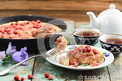 Homemade rhubarb pie in cast iron skillet with fresh wild strawberries on shabby turquoise boards with tea and bellflower Stock Photo