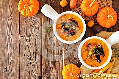 Homemade roasted autumn vegetable soup in onion soup bowls, top view corner border on a rustic wood background with copy space Stock Photo