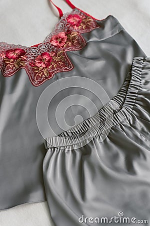 homemade silk pajamas lying on the bed without anyone. gray pajamas with red lace on a beige background Stock Photo