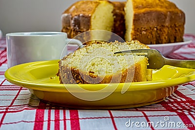 Homemade simple cake. Detail of homemade cake slice being cut with fork on a yellow plate with cup of coffee and cake in the backg Stock Photo