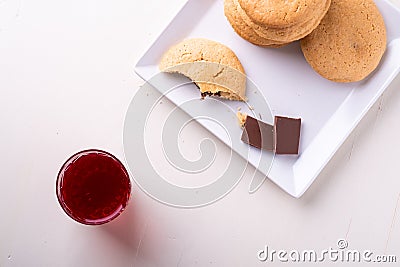 Homemade stack of shortbread chocolate cookies with one bitten cookie and two pieces of chocolate on white plate with stewed fruit Stock Photo
