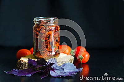 Homemade sun-dried tomato slices in glass jar in olive oil, basil, oregano spices, red pomodoro on dark background. Stock Photo