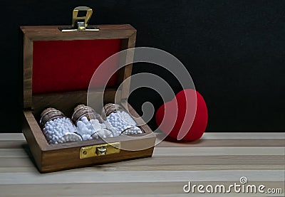 Homeopathy â€“ Close view of homeopathy medicine bottles in wooden classic box on wood surface with red heart on dark background Stock Photo
