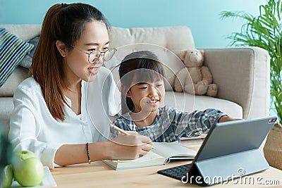 Homeschooling. Asian family with daughter doing homework by using tablet with mother help. Asia mom and child learning online with Stock Photo