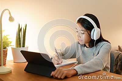 Homeschooling, Asian girl doing homework and online learning with tutor on the tablet digital with headphones at home night Stock Photo