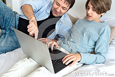 Homeschooling, home education concept. Father and teenager son looking at laptop screen, wathing video or communicate online in Stock Photo