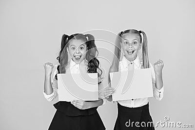 Homework done. Happy small children holding empty homework sheets on yellow background. Cute little girls smiling with Stock Photo