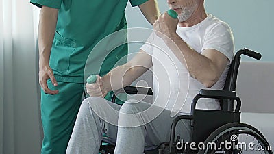 Homme supérieur dans le fauteuil roulant fléchissant des bras avec des haltères, aidées par l'infirmière, réadaptation Homme supérieur dans le fauteuil roulant fléchissant des bras avec des haltères, aidées par l'infirmière, réadaptation