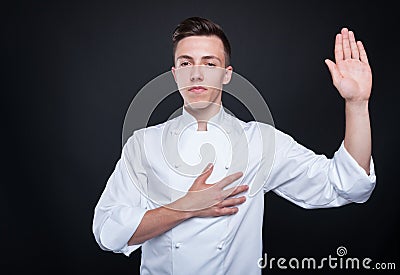 Honest cook rising his left hand and swearing Stock Photo