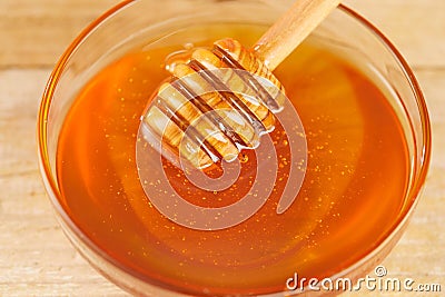 Honey dripping from honey dipper in glass bowl. Thick honey dipping from the wooden honey spoon, closeup. Stock Photo