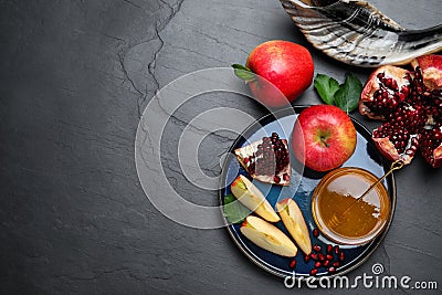 Honey, pomegranate, apples and shofar on black table, flat lay with space for text. Rosh Hashana holiday Stock Photo