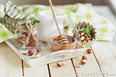 Honey in the wooden bowl, mint leaves, hazelnuts and jar with milk on the wooden tray Stock Photo