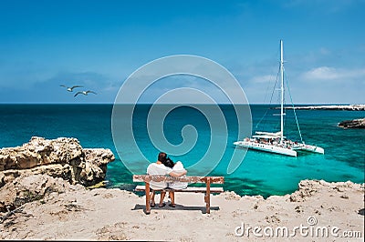 Honeymoon traveller couple hugging on a wooden bench and enjoys their tropical holiday Stock Photo