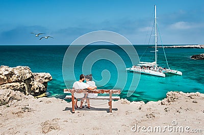 Honeymoon traveller couple hugging on a wooden bench and enjoys their tropical holiday Stock Photo