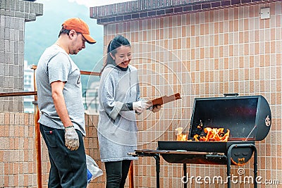 Hong Kong, China - January 17, 2016: Young couple of Caucasian man and Asian woman kindle fire on barbecue. Outdoor barbecue cooki Editorial Stock Photo
