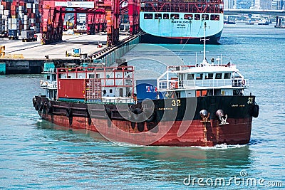 Small barge loaded with cargo containers sailing away from port terminal. Editorial Stock Photo