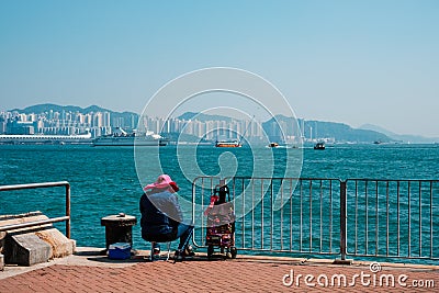 Fisher man or woman with fishing rod sitting on coast with HongKong skyline background Stock Photo