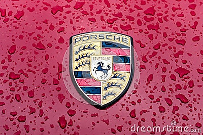 Hood emblem of sports car Porsche in raindrops on the burgundy background. Editorial Stock Photo