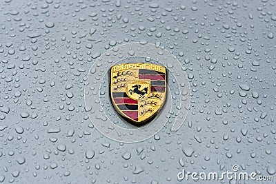 Hood emblem of sports car Porsche in raindrops on the grey background. Editorial Stock Photo