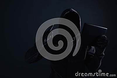 Hooded computer hacker with obscured face using digital tablet Stock Photo