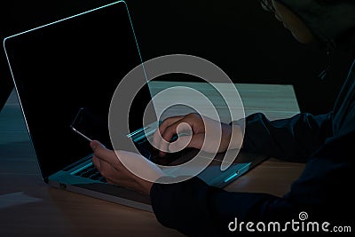 Hooded cyber crime hacker using mobile phone internet hacking in Stock Photo