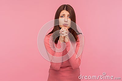 Hopeful brunette woman in pink sweater holding hands in prayer, asking for forgiveness looking at camera with regard, need help Stock Photo