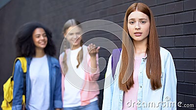 Hopeless bullying victim looking camera, female classmates discussing behind Stock Photo