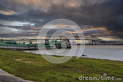 The Horace Wilkinson Bridge over the flowing waters off the Mississippi River with boats on the water, lush green grass and clouds Stock Photo
