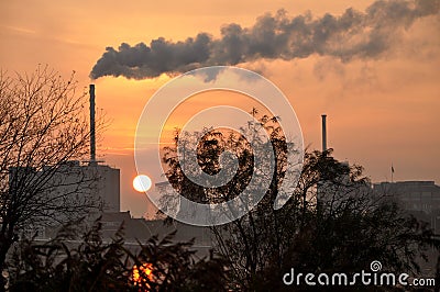 Horizon industry in a small netherland town in Europe, with a big chimney and smoke, sunset and sun as background Stock Photo