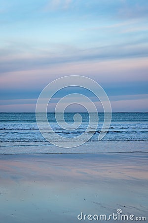 Horizon with waves and brightly coloured sunset reflected in wet, sandy beach, Scotland Stock Photo