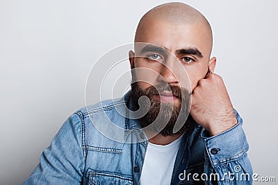 A horizontal close-up of handsome bald man having charming dark eyes, thick black eyebrows and beard wearing jean shirt holding hi Stock Photo