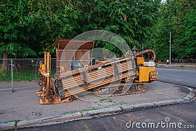 Horizontal Directional Drill. The orange drilling rig stands on the city square. Dark asphalt and trees in the background Stock Photo