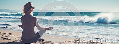 Horizontal image rear view young blond woman sitting in lotus position folded fingers mudra gesture meditating on the beach Stock Photo