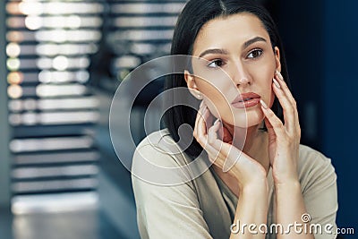 Horizontal indoor portrait of beautiful young lady with natural makeup examining her face while looking into the mirror Stock Photo