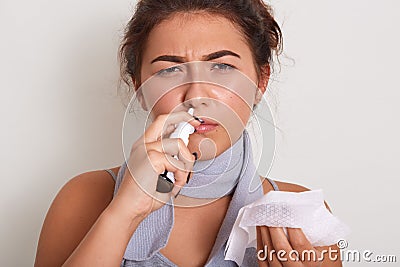Horizontal indoor studio shot of bad looking woman having caught cold, feeling unwell, being on sick leave, using nose spray, Stock Photo