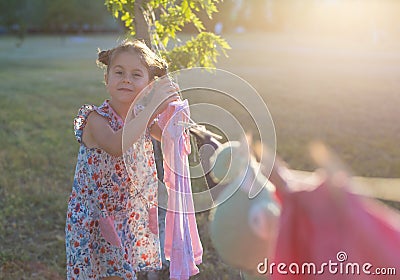 Horizontal photo of a six-year-old pretty girl who hangs washed clothes Stock Photo