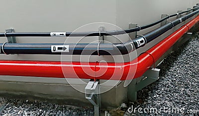 Horizontal pipeline in black and red color installed hanging along outside at building wall, showing engineering utility design Stock Photo