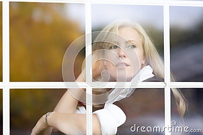 A horizontal portrait of Caucasian woman with long blond hair behind a window glass, dreamy Stock Photo