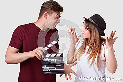 Horizontal shot of cheerful woman and man look positively at each other, gesture actively, have hesitant expressions, holds Stock Photo