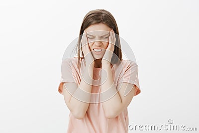 Horizontal shot of intense bothered cute woman feeling headache or migraine, touching temples, clenching teeth Stock Photo