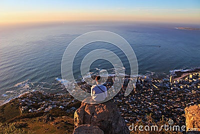 Horizontal shot of a man sitting on the edge of the rock and looking at the coastline city Editorial Stock Photo