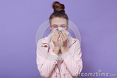 Horizontal shot of sick teenage girl with hair bun wearing casual attire, poses isolated over lilac studio background, woman uses Stock Photo