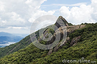 Horizontal view of a mountain rock face with some trees under a blue sky with white clouds - pico e serra do lopo Stock Photo