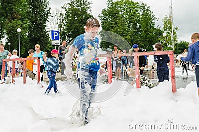 HORKI, BELARUS - JULY 25, 2018: A little fair-haired boy plays with airy white foam at the Rescue Service 112 holiday amid a crowd Editorial Stock Photo